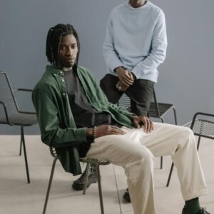 Portrait of two stylish African American men sitting indoors, showcasing modern fashion.